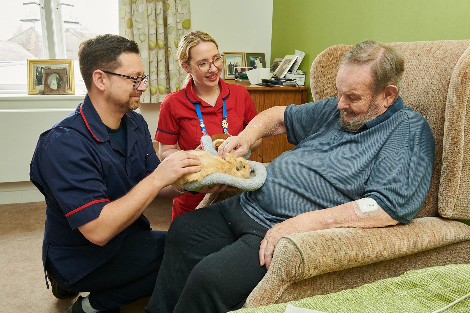 A member of staff and a nurse introducing a resident to a guinea pig during a pet therapy session