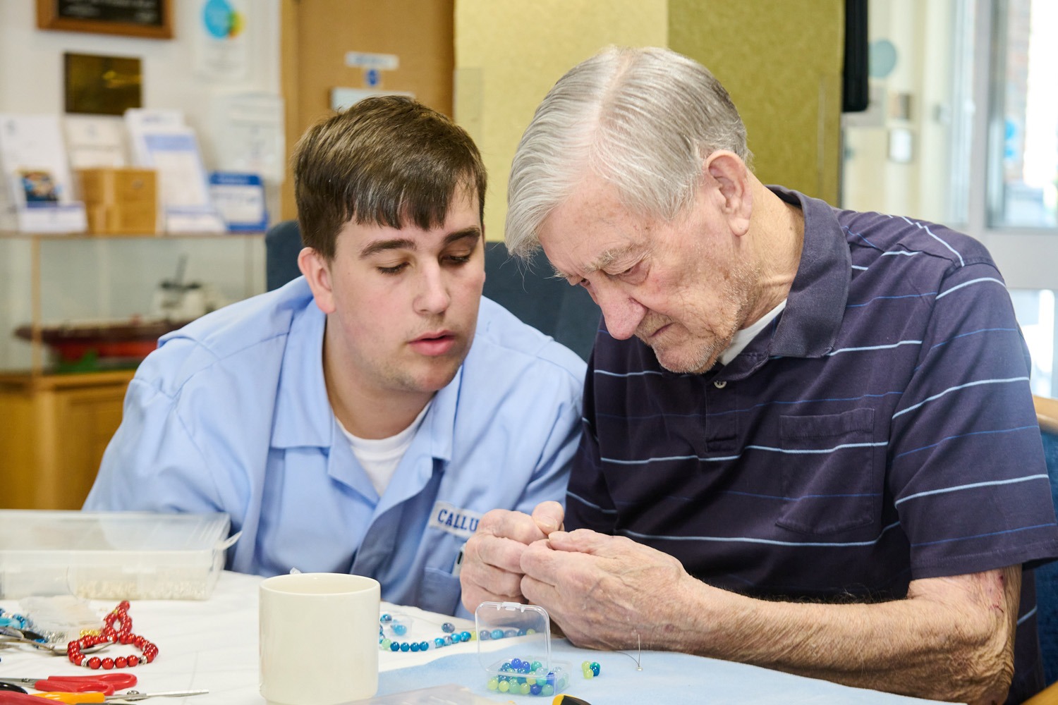 A member of staff helping a resident with a beading craft activity