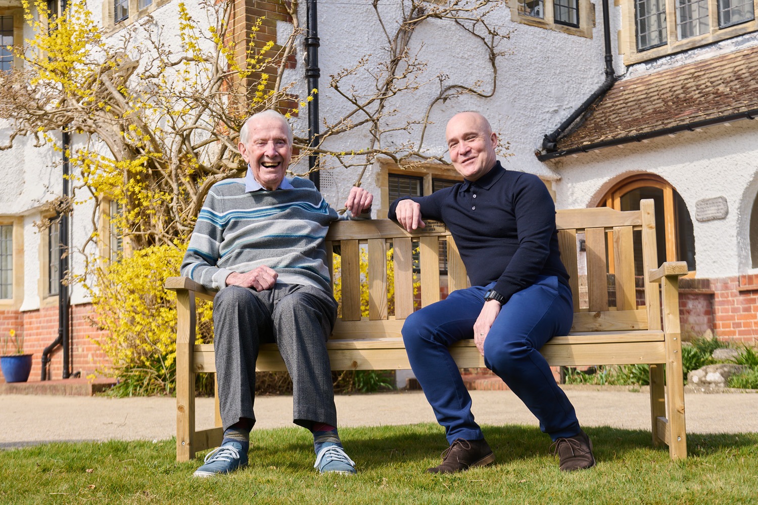 Two residents relaxing together on a bench in the grounds at Weston Acres